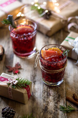 Glasses of mulled wine, christmas hot drink with berries and citrus fruits on wood table with gift boxes 