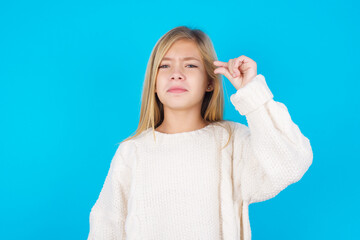 Upset caucasian little kid girl wearing wool jersey over blue background shapes little gesture with...