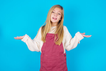 So what? Portrait of arrogant caucasian little kid girl wearing jumpsuit over blue background shrugging hands sideways smiling gasping indifferent, telling something obvious.