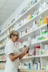 Beautiful senior female pharmacist checking medications on a shelf