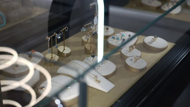 High angle view fine jewellery on holders on showcase in shop. Luxurious precious beautiful accessories for sale in jewelry store indoors. Slow motion