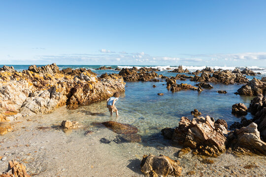 Young boy exploring a beach and rockpools on a jagged rocky coastline. 