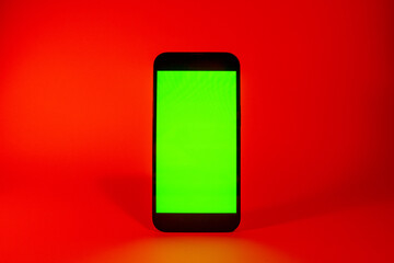 Mobile phone with green screen, smartphone mock up. Danger and attention concept, red illumination. Flat screen modern smartphone