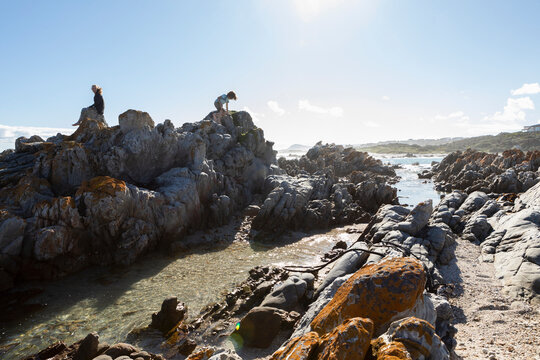 Two children, a teenage girl and eight year old boy exploring the jagged rocks and rockpools on a beach.