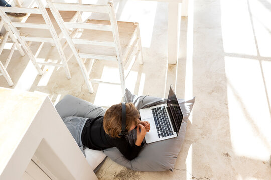 Eight year old boy lying on the floor on cushions using a laptop