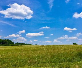 Green field hillside extends under a blue sky with white fluffy clouds