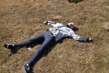 resting teenage girl lying on the ground with outstretched arms on a plateau in the mountains