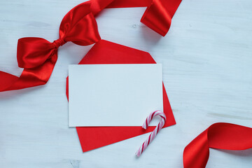 Blank white card, red envelope and candy cane on white wooden background with soft bokeh. Festive stock photo