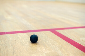 the squash ball lies on the wooden floor between the lines dividing the squash zones