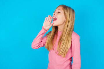caucasian little kid girl wearing long sleeve shirt over blue background look empty space holding hand near her face and screaming or calling someone.