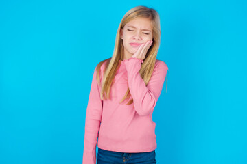 caucasian little kid girl wearing long sleeve shirt over blue background with toothache