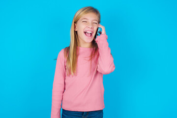 Overemotive happy caucasian little kid girl wearing long sleeve shirt over blue background laughs...