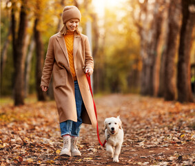 Happy smiling woman walking her cute golden retriever puppy in forest on beautiful fall day