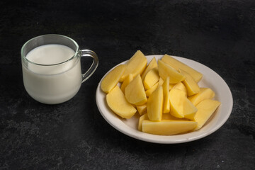 Potato milk on a black background. A glass of milk and a plate of raw potatoes.