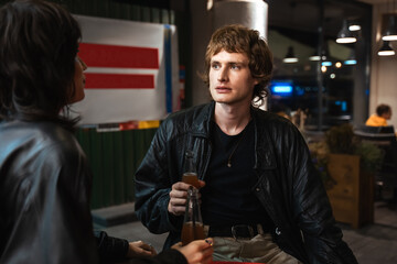 Caucasian man holding glass bottle with cola and telling something to his girlfriend