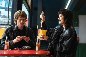 Girl eating noodles while her boyfriend rolls a cigarette at the evening street cafe