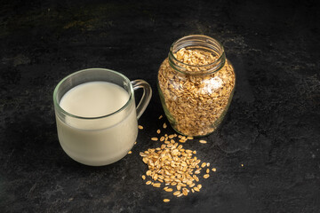 A glass of oat milk and oatmeal on a black background.