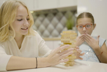 Obraz na płótnie Canvas two girls have fun playing Jenga together - board game to remove wooden blocks and kids leisure concept