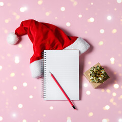 New year wish list concept. Notepad, Santa Claus hat isolated on pink background. Holiday banner with copy space