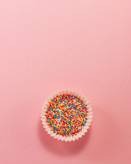 Cupcake liner with colored sugar inside at the bottom from above. Flat lay top view. Confectionery cooking concept on bright pink paper background National cooking day.