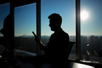 Successful businessman boss working at computer on the background of large windows, silhouette