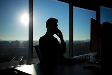 Successful businessman boss working at computer on the background of large windows, silhouette - Powered by Adobe