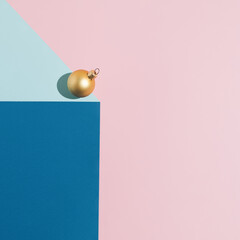Christmas and New Year ornament idea with a golden bauble with blue and pink background. Festive winter decoration concept. Minimal geometric visualization.