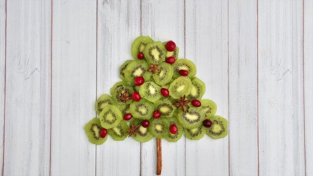 Animation of kiwi slices and holiday spices forming a Christmas tree with Merry Christmas message
