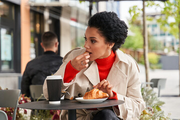 Brunette woman eating croissant while resting at the street cafe