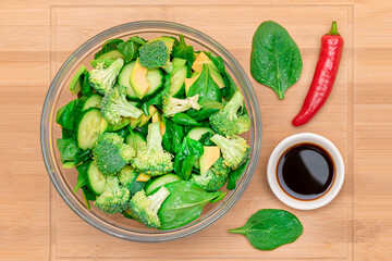 Fresh Green Salad of Avocado, Broccoli, Spinach and Cucumber with Soy Sauce and Red Hot Pepper on Wooden Cutting Board. Vegan Salad. Vegetarian Culture. Raw Food. Healthy Eating and Vegetable Diet