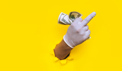 Fuck you gesture. A young doctor holds money in white medical gloves. Isolated. Yellow torn hole...