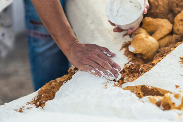 Female hand spreading white paste on the rough surface of a polystyrene figure.