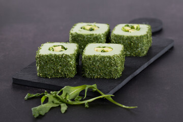Sushi avocado, square rolls with finely chopped greens on a serving board on a dark gray background
