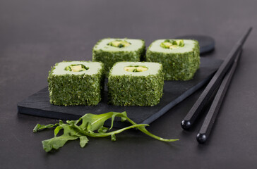 Vegan dish, avocado sushi, rolls with finely chopped greens on a serving board on a dark gray background