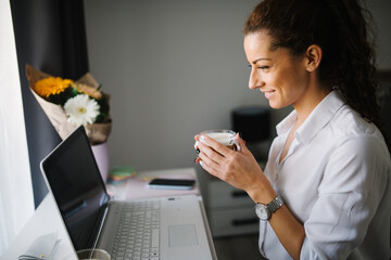 Woman looking at he laptop and smiling while holding a cup of co