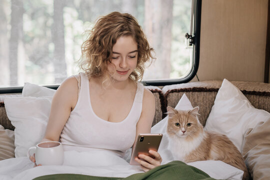 Woman and ginger red cat in trailer with phone.