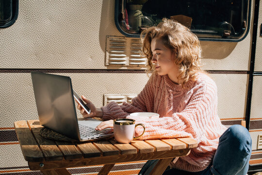 Woman at laptop with phone working near trailer.