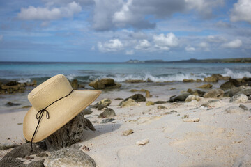 Straw hat lying on the sandy beach with corals. Seascape.