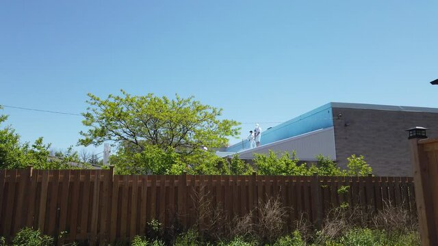 Wider Angle Shot Maitenance Workers In Light White Clothing Power Washing Top Of New Bilding While Standing On Rooftop