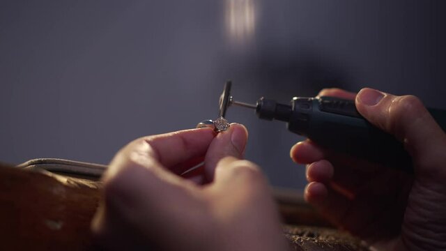 Close-up silver ring with gemstone in female hands polishing jewellery. Unrecognizable skilled professional Caucasian young woman making luxurious expensive accessory in workshop with blue light