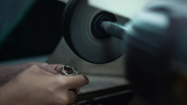 Close-up female hands polishing silver ring with equipment in workshop. Unrecognizable Caucasian silversmith repairing creating jewellery in slow motion indoors. Beauty and luxury