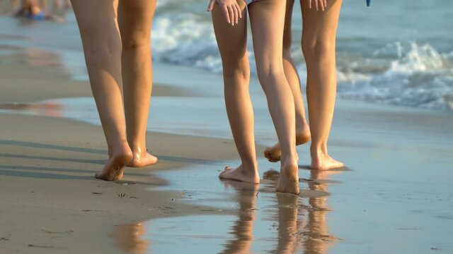 Family walking on the sea shore with the waves splashing on the sandy beach, closeup of people's legs walking on the beach