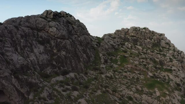An aerial shot of a flight through a large gray stone cliff for which a wonderful cityscape of a Central Asian city opens. Urban landscape, a city at the foot of a mountain. daytime, 4k drone