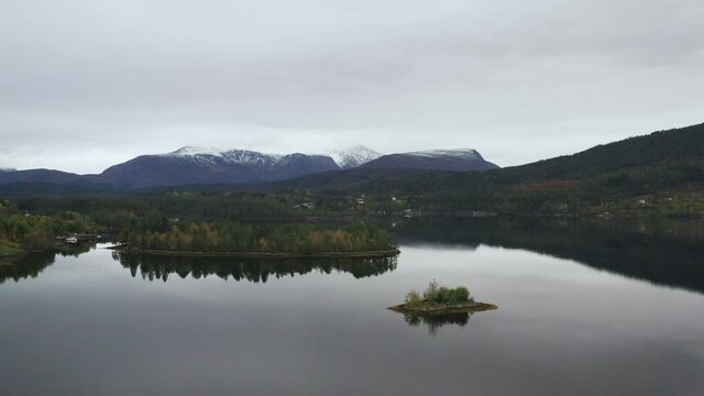 Calm Lake With Small Islands And Mountain Snowy View in The Background, Norway. - Aerial, pull in 