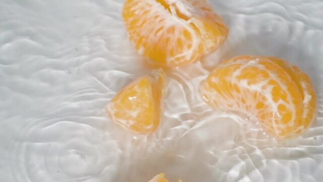 Close up Peeled Mandarin orange Falls into Water breaks up into slices, white Background 