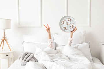 Morning of young woman with clock lying in bed