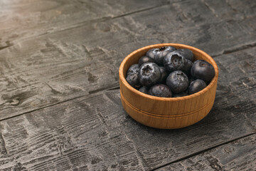 A small wooden bowl with blueberries on a rustic table.
