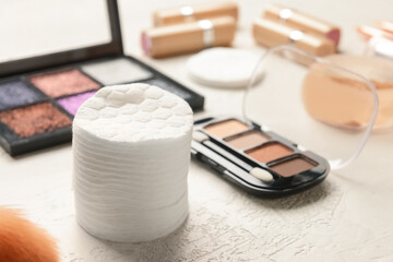 Stack of soft cotton pads and decorative cosmetics on light table, closeup