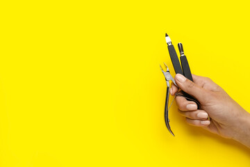 Female hand with manicure instruments on yellow background