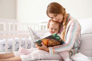 Young mother reading book to her cute little baby on bed